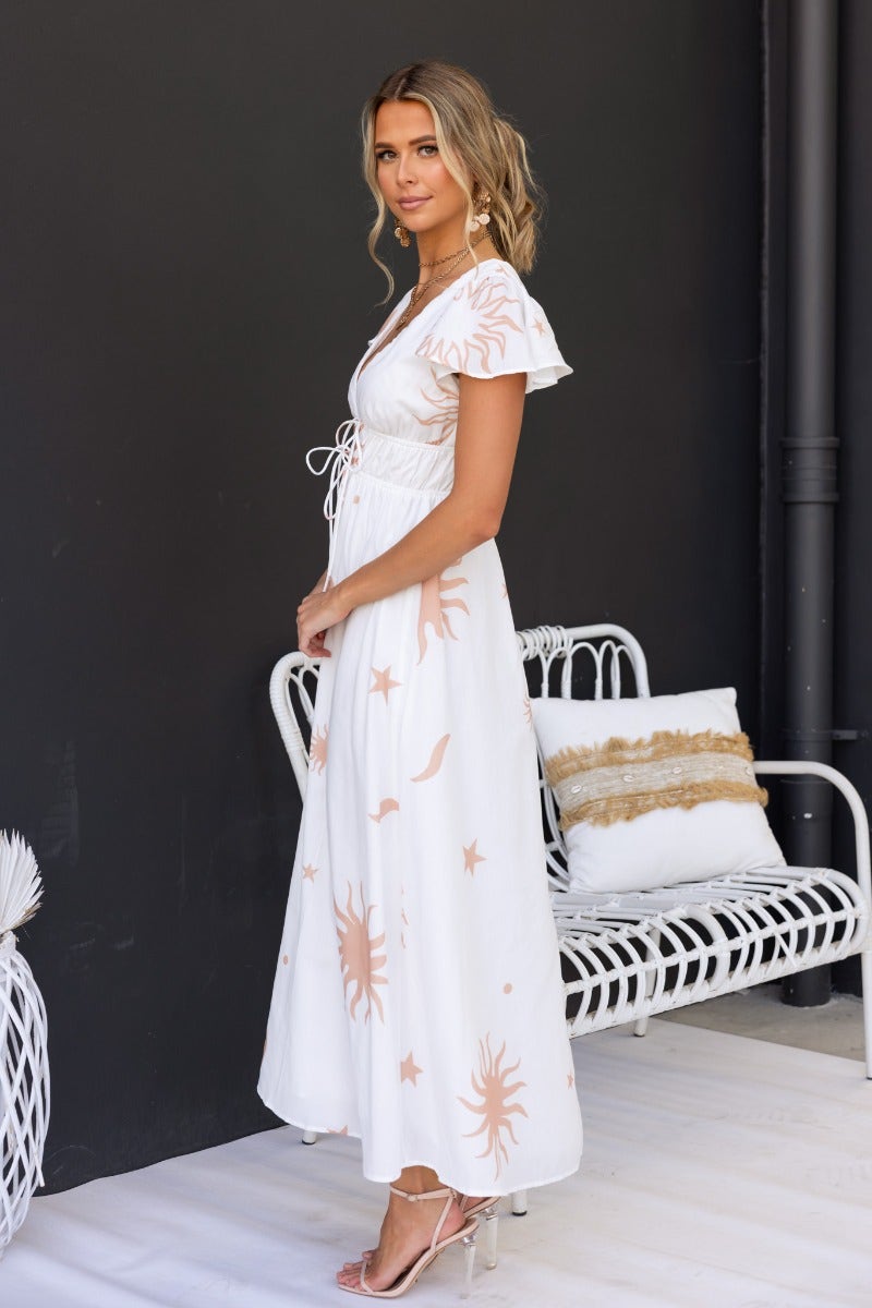 Model wearing a white Milene Maxi Dress with tie detail and sun pattern, showcasing its flowy design and V-neckline.