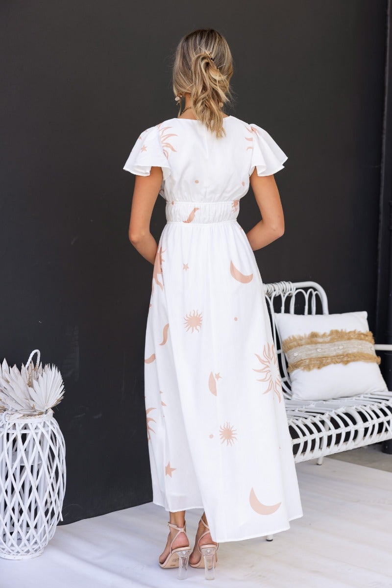 Back view of a model wearing a white Milene Maxi Dress with sun and moon prints, featuring flutter sleeves and an elastic waistband.