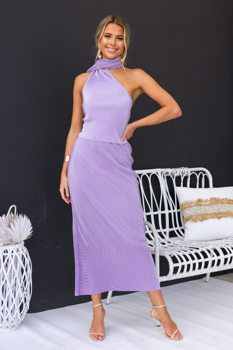Stylish woman wearing a lavender Amethyst top with accordion pleats and high wrap neckline, posing elegantly.