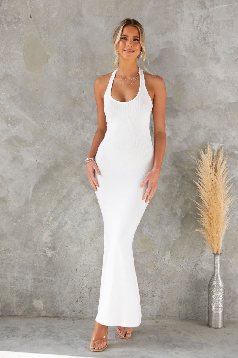 Model wearing a ribbed white maxi dress with a halter neckline, set against a textured gray background.