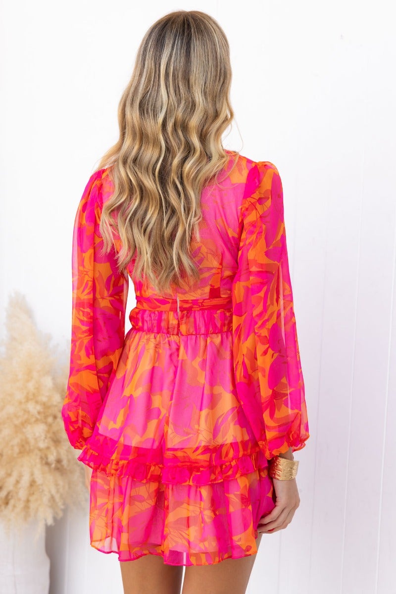 Back view of a floral print vanity dress in pink and orange with elastic sleeves and ruffled hem.
