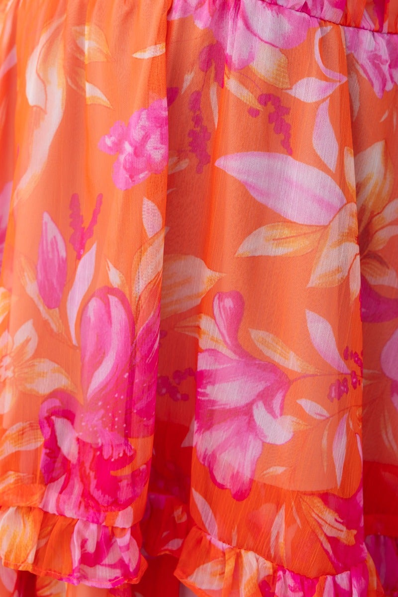 Close-up of vibrant floral print in orange and pink on a dress, showcasing lightweight fabric and ruffled hem.