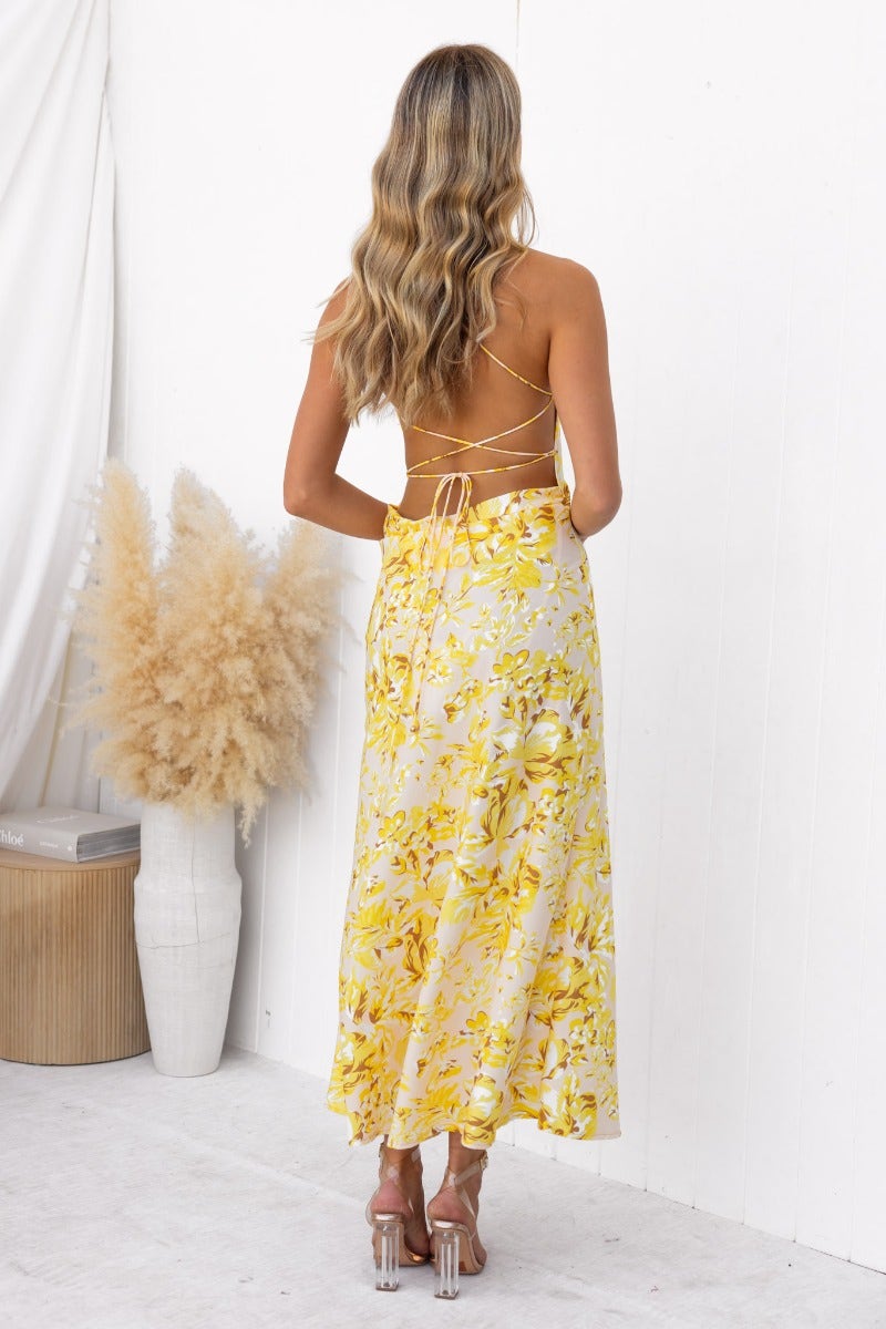 Back view of the Ambra Maxi Dress featuring adjustable tie straps and a vibrant floral print in yellow hues.