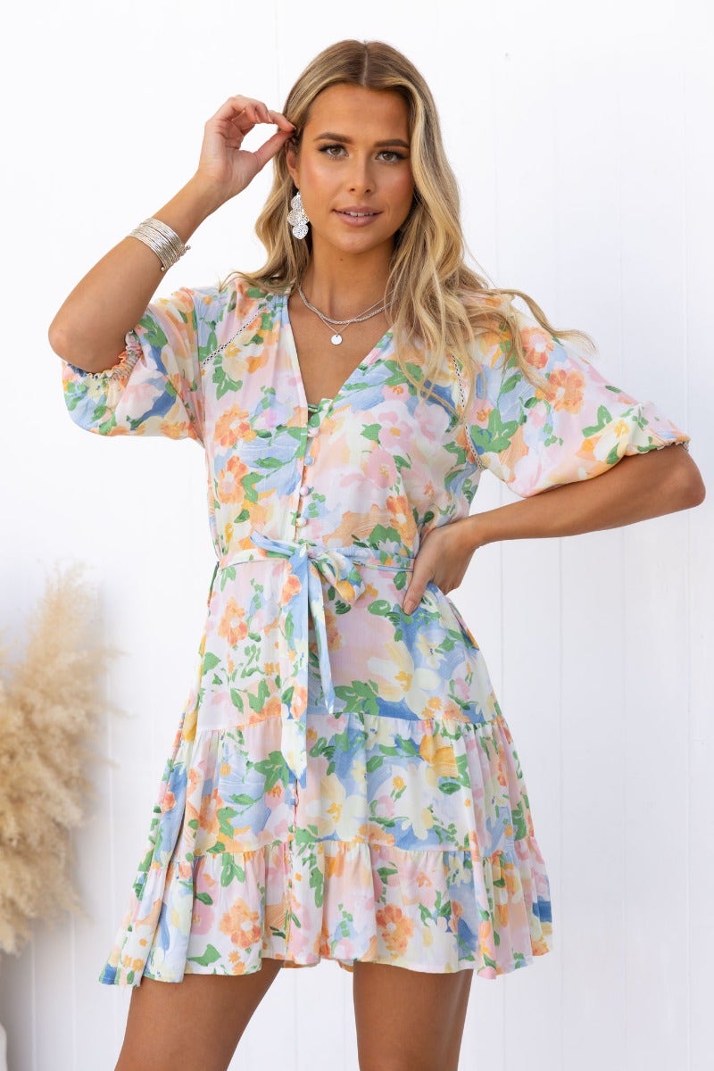 Model wearing a floral print Harbin dress with V-neckline, button-up front, and removable belt against a white background.
