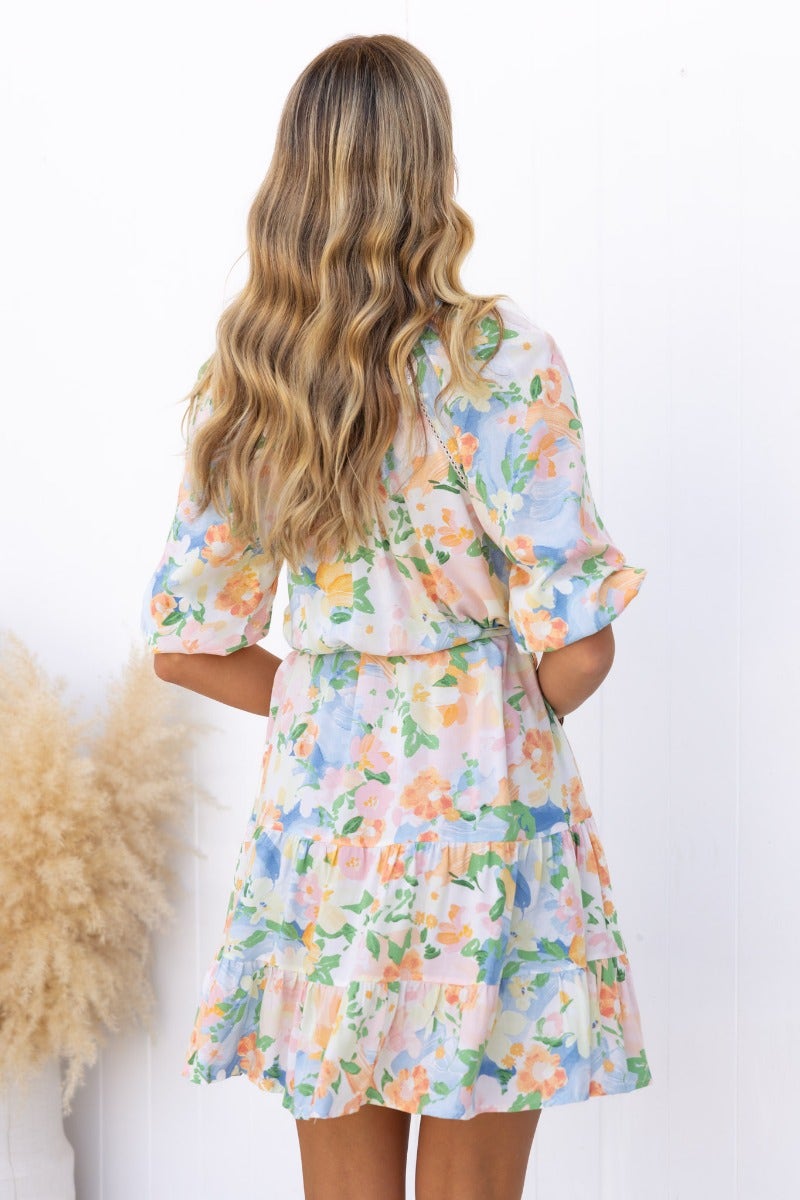 Back view of a woman in a floral print Harbin Dress with V-neckline and ruffled hem, styled with wavy hair.