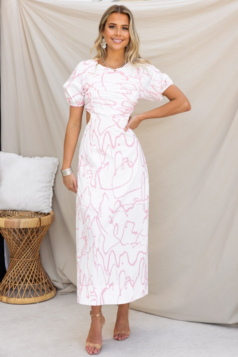 Model wearing Jaida Maxi Dress, a white cotton dress with pink abstract lines, showcasing cut-out waist and puff sleeves.