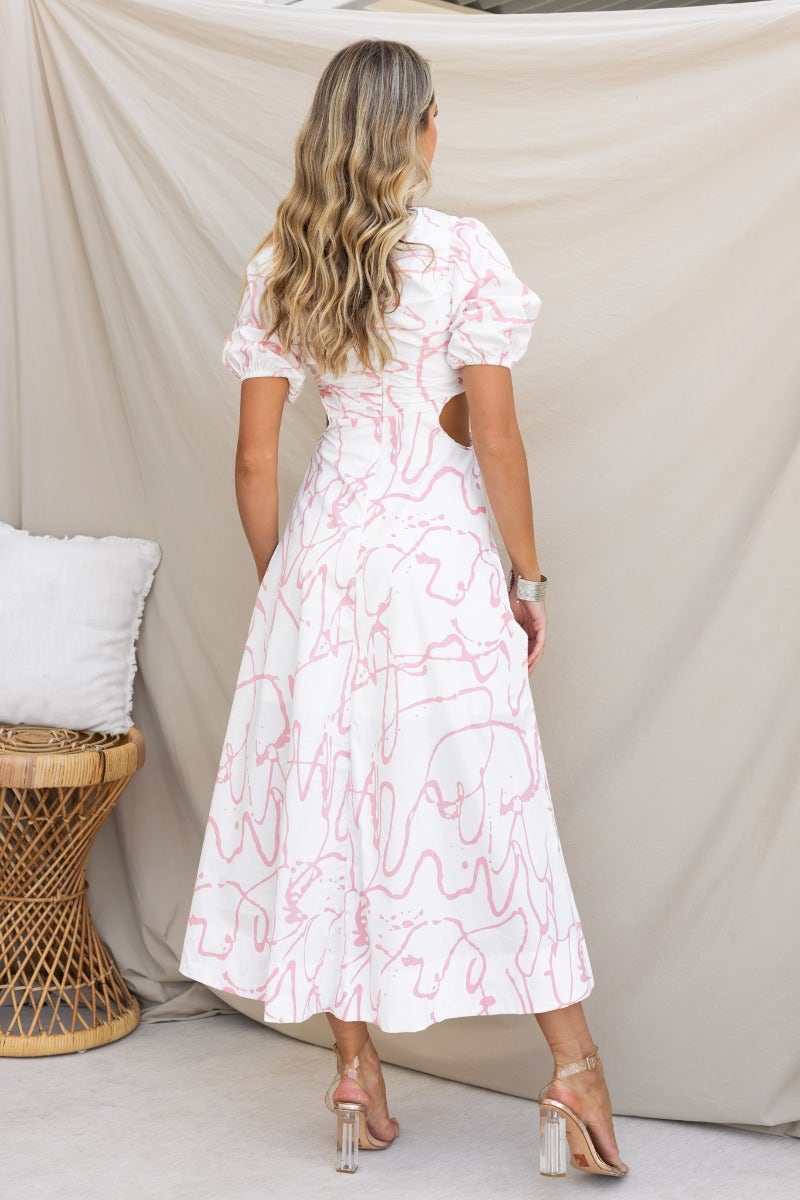 Back view of a woman wearing a Jaida Maxi Dress with cut-out waist and puff sleeves, showcasing a white fabric with pink abstract design.