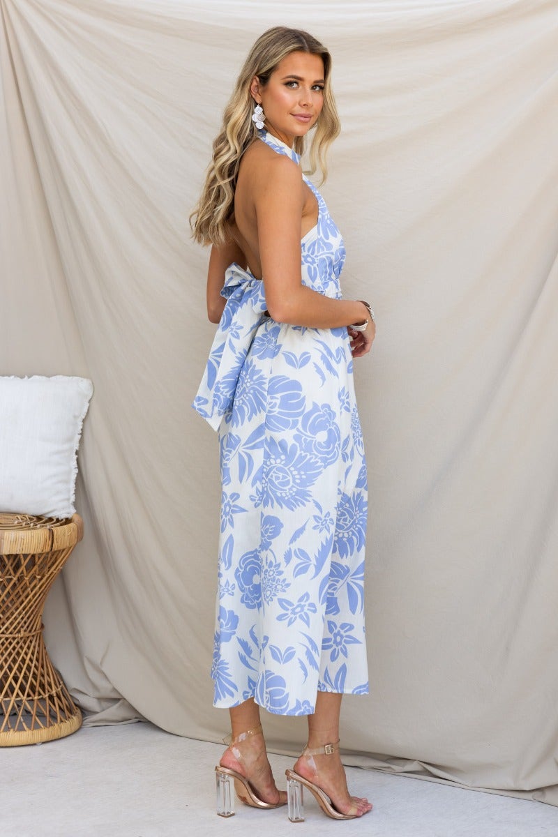 Corio Midi Dress in light blue floral print, featuring a tie halter neckline and back bow detail, styled with heels.