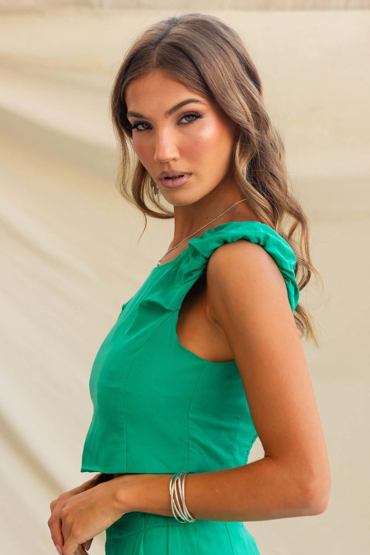 Model wearing a vibrant green cropped top with a boat neckline and ruffled straps, styled for a chic summer look.