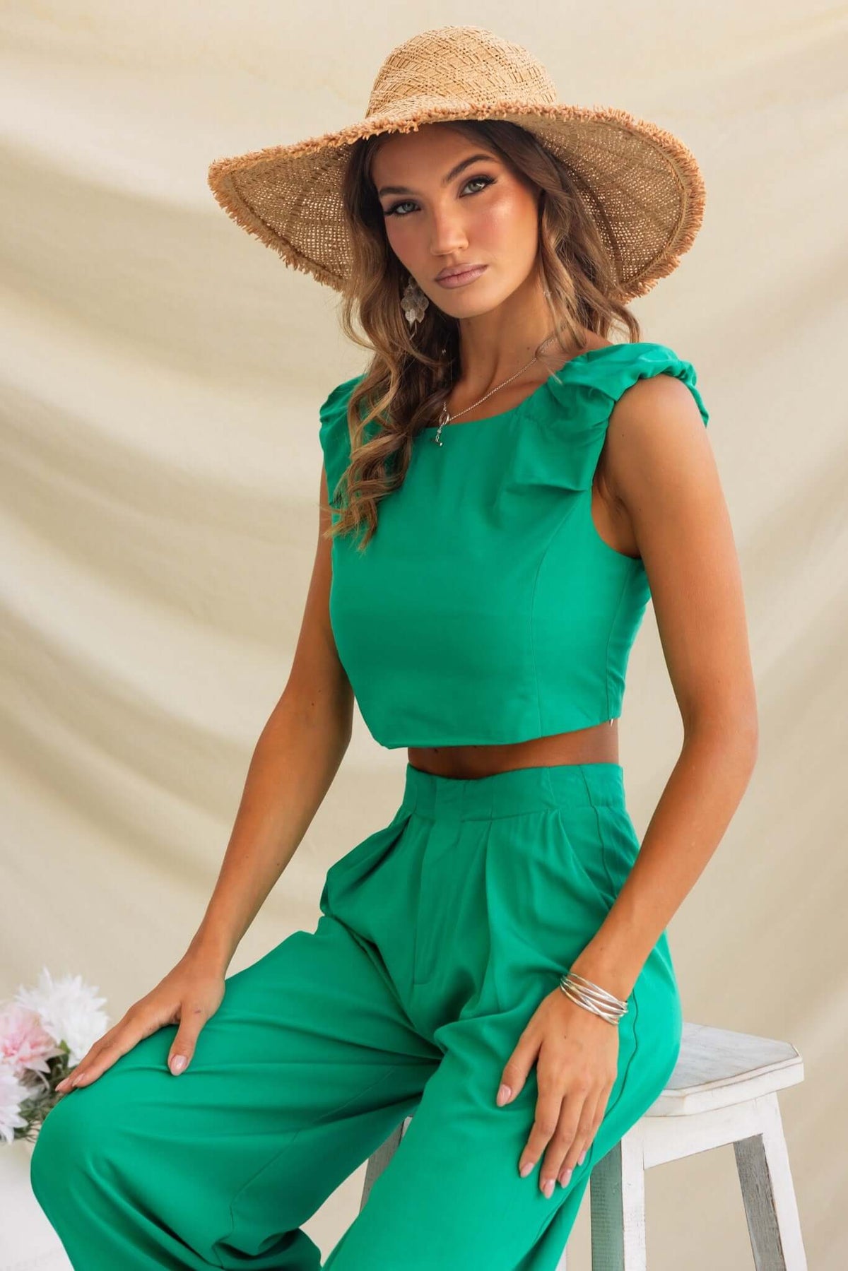 Model wearing a green Erik Top with boat neckline, paired with matching pants and a straw hat.