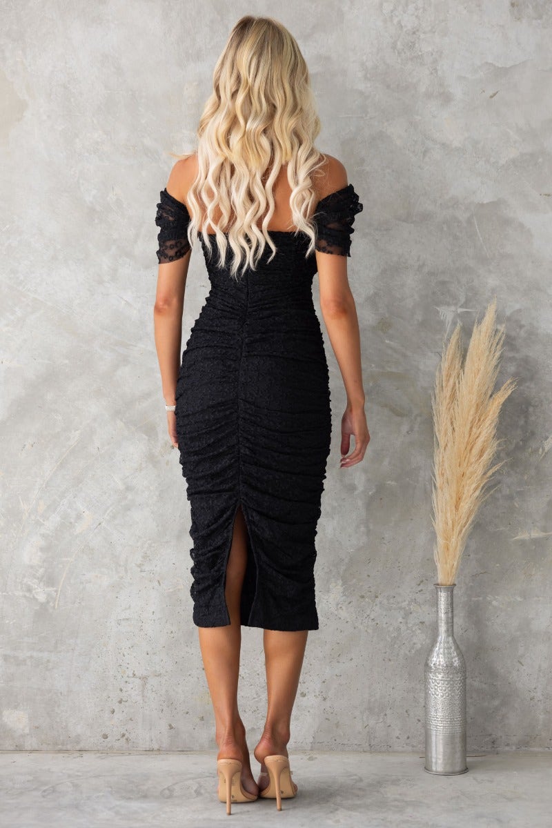 Back view of a black bodycon midi dress with off-shoulder sleeves, ruching, and a back split detail.