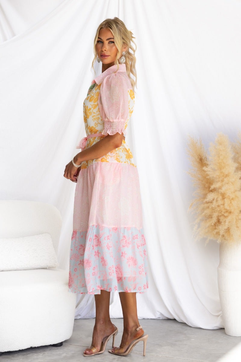 Side view of a woman in a floral print Connie Midi Dress with puff sleeves and a tiered skirt against a neutral backdrop.