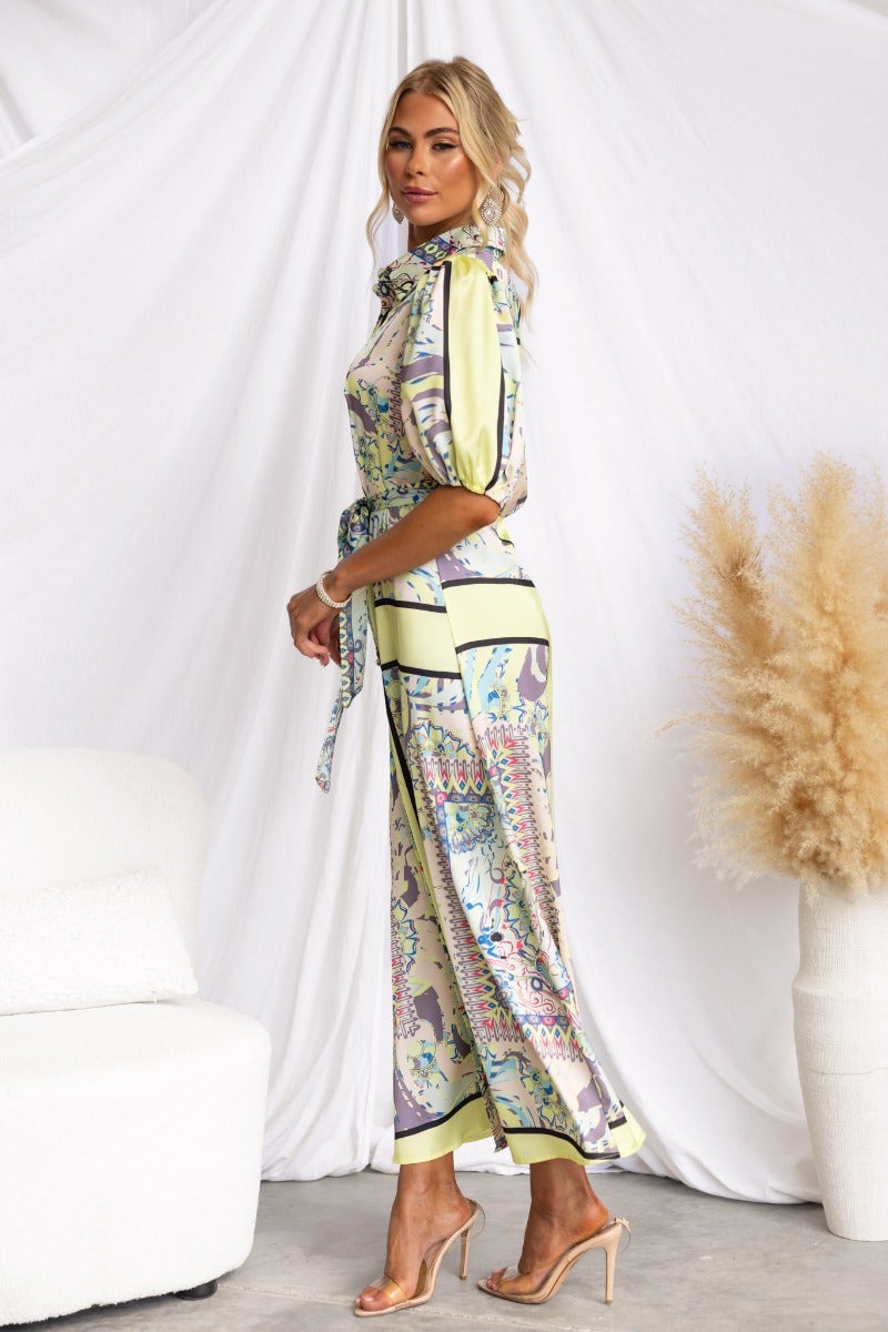 Side view of a woman in a Nicosia Maxi Dress with an abstract print, featuring a collar and removable tie.