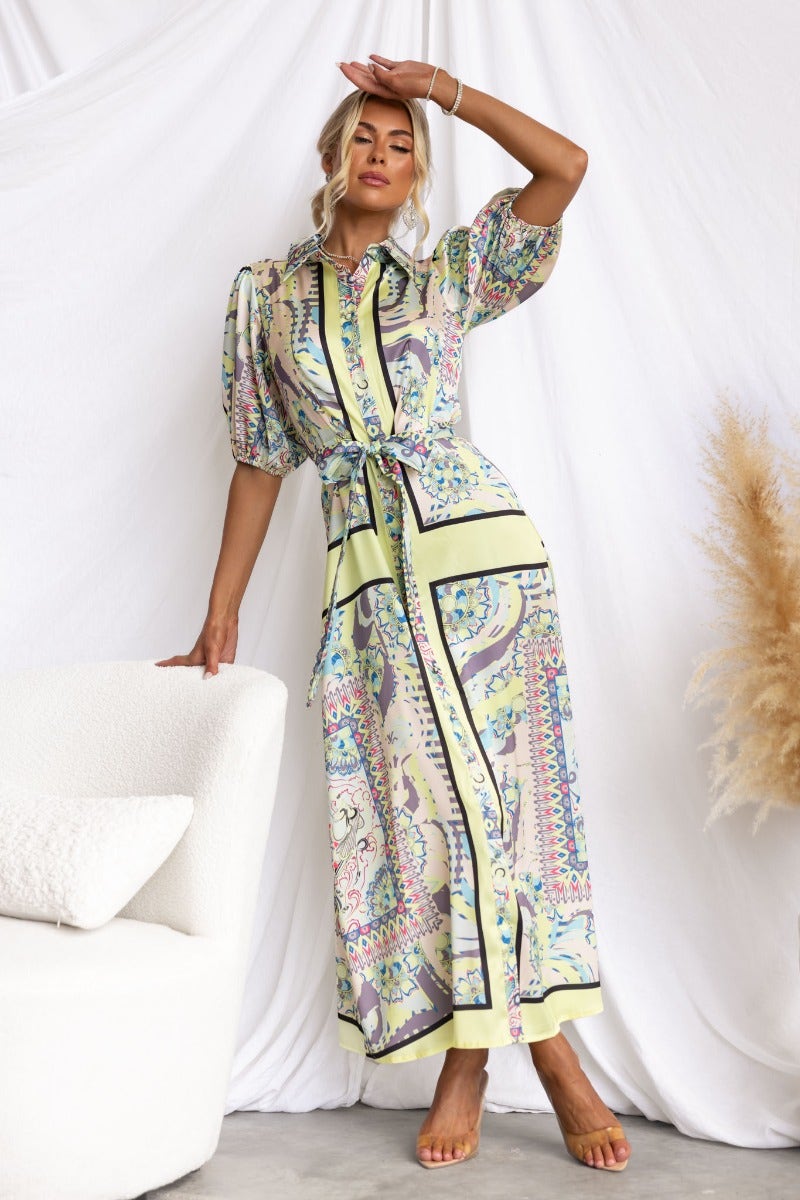 Nicosia Maxi Dress with abstract print, button-up front, and removable tie, featured in a stylish setting.