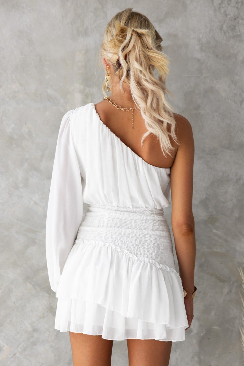 Back view of a model in a white mini dress featuring a one-shoulder design and ruffled hemline.