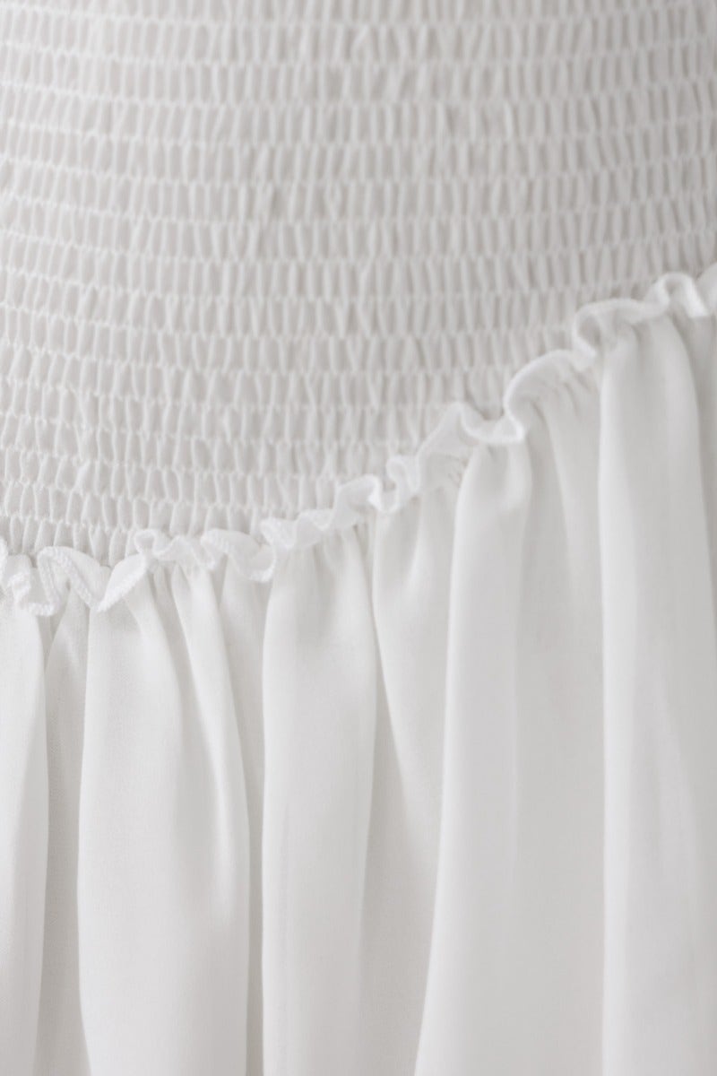 Close-up of the white Be The Light Dress featuring smocked bodice and delicate ruffled hem.