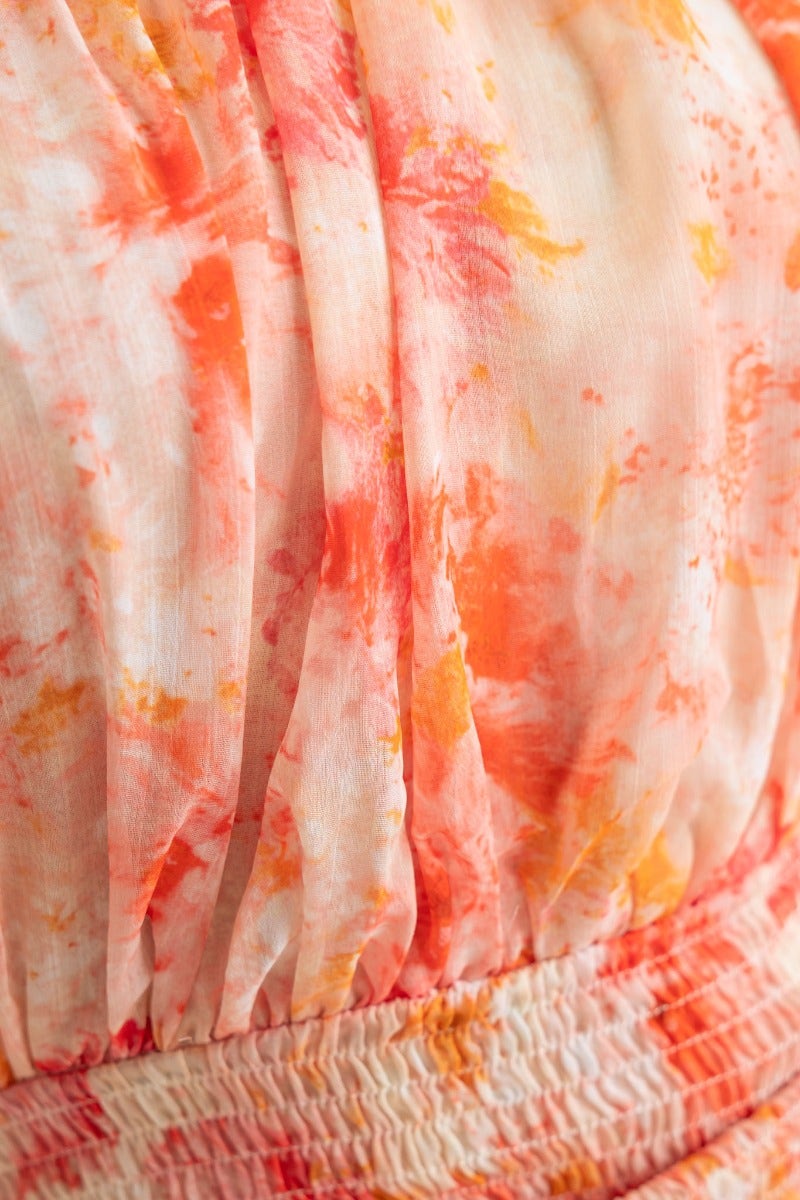 Close-up of the floral print fabric featuring soft orange and pink hues, showcasing the draping and elastic waist of the dress.