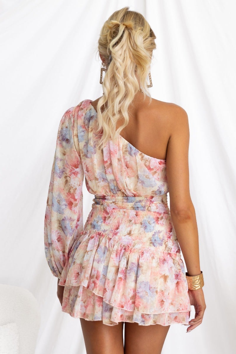 Back view of a floral print one-shoulder dress featuring elastic cuffs and a ruffled skirt.