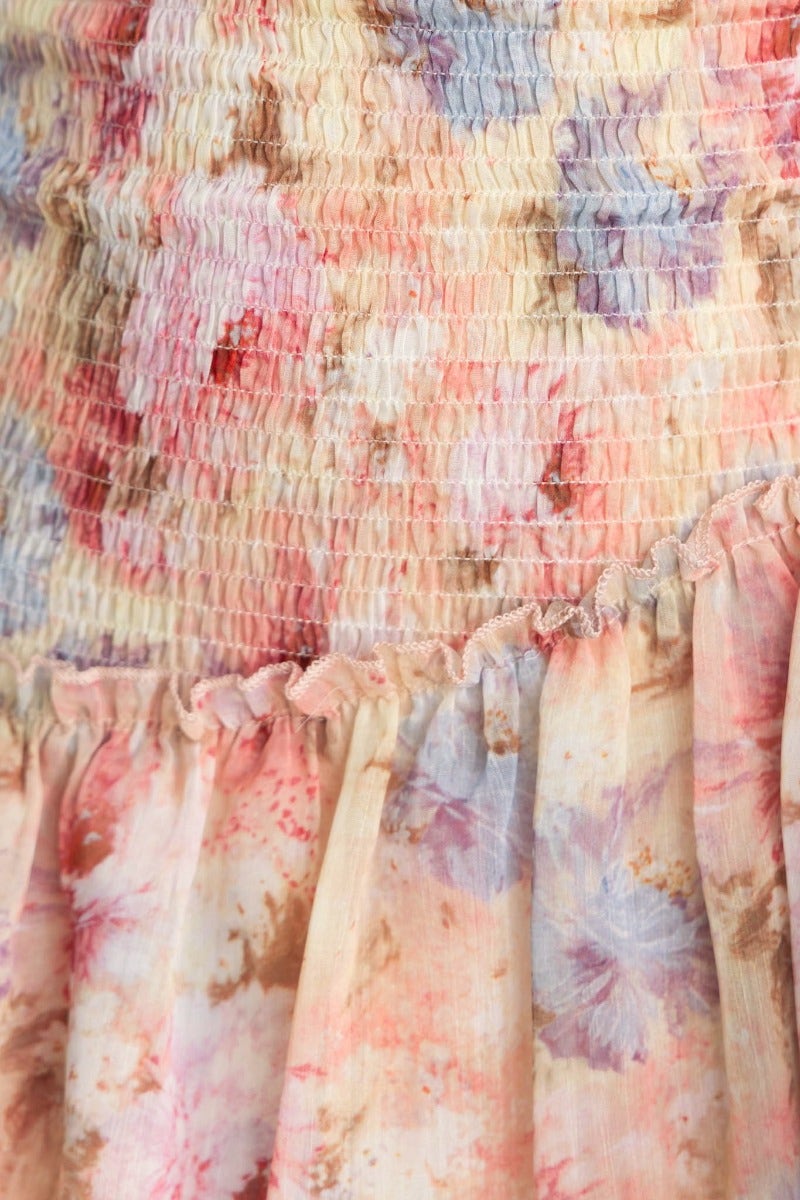 Close-up of floral print fabric featuring soft pink and blue hues, showcasing the gathered texture and ruffled hem of the dress.