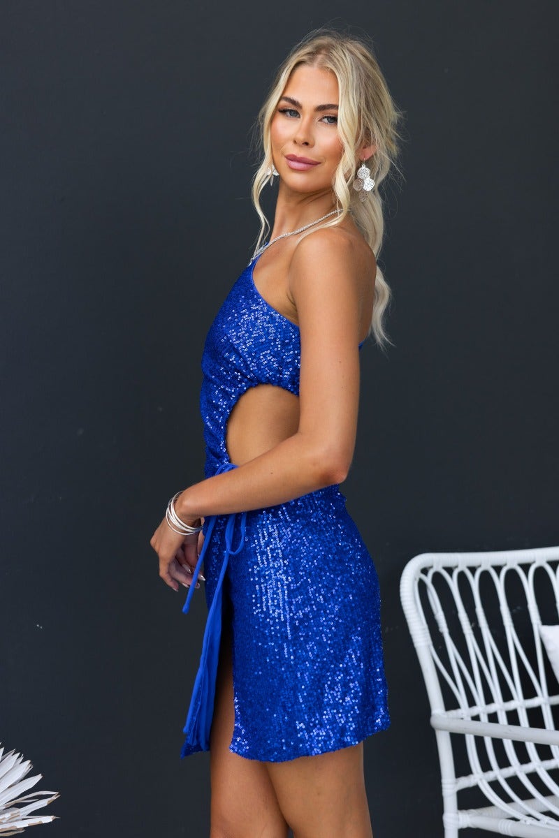 Keesha Dress in blue sequin with one-shoulder neckline and cut-out waist, styled for a chic look.