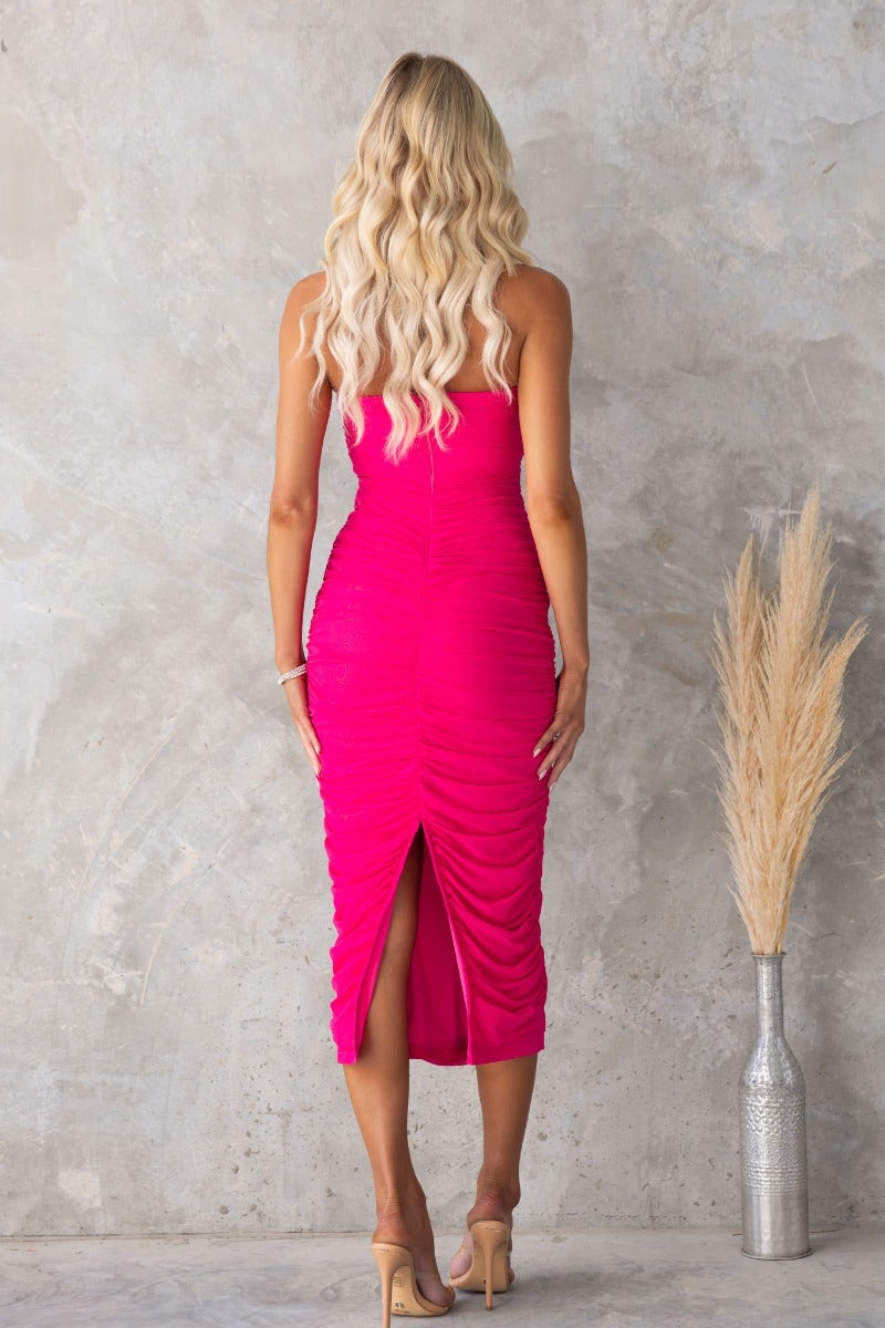 Back view of a pink bodycon midi dress with ruching and a back split, showcasing its stylish design and strapless silhouette.