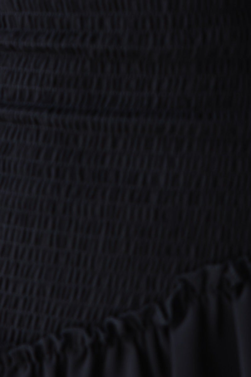 Close-up of the textured fabric of the black Be The Light mini dress, showcasing the smocked detail and ruffle hem.