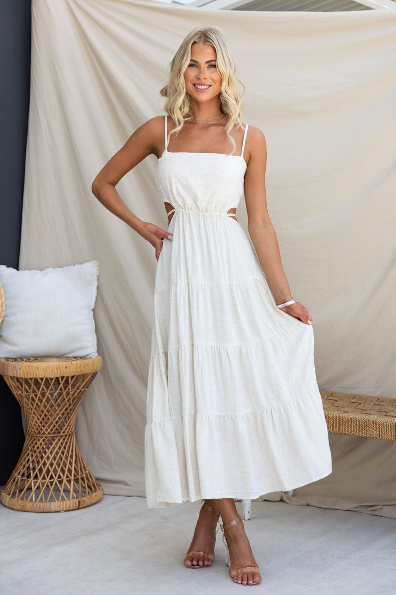 Brookman Midi Dress featuring adjustable straps, cut-out waist, and linen texture, modeled by a woman in a stylish setting.