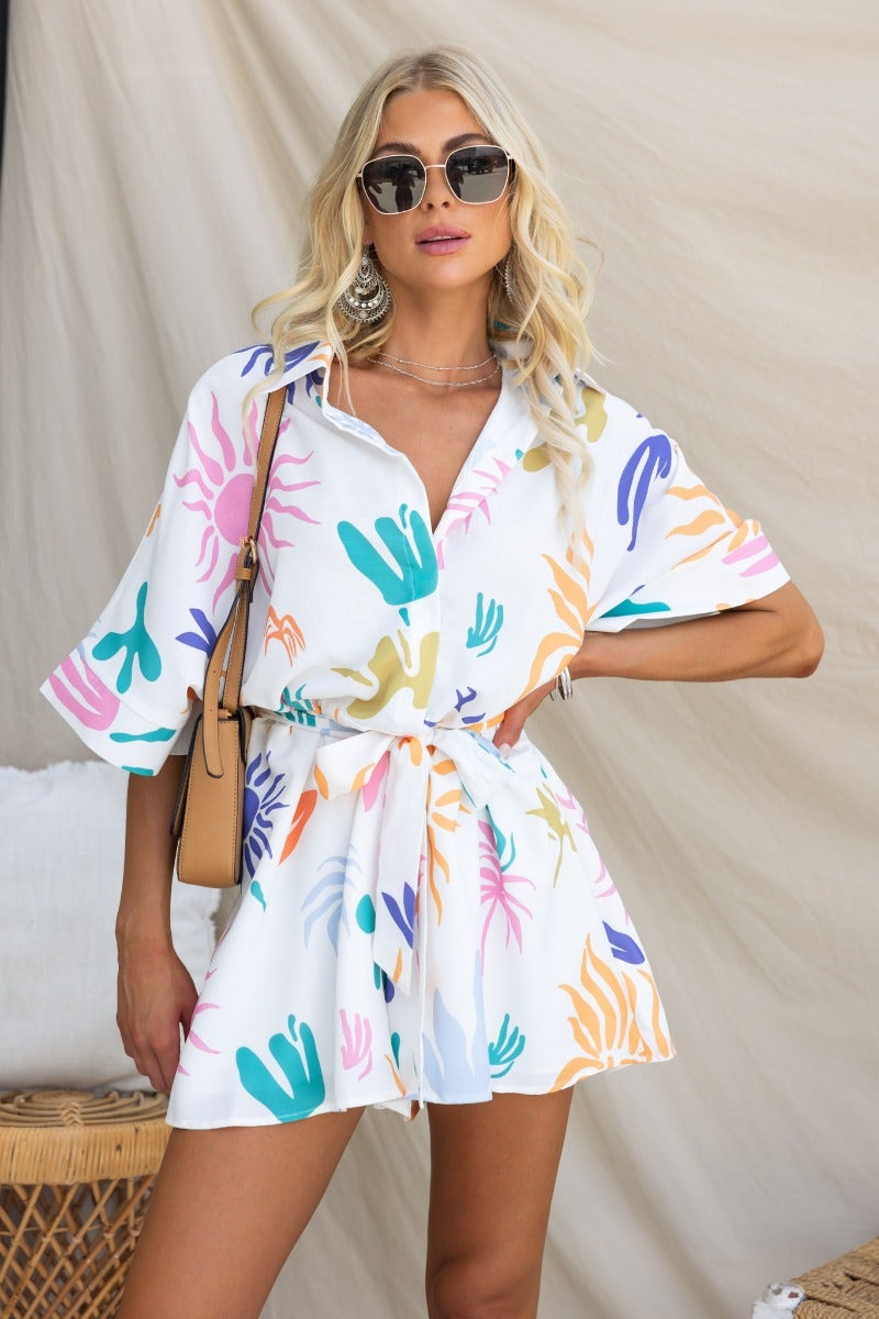 Model wearing the Leonie Playsuit with abstract print, button-up collar, and removable fabric tie, styled with sunglasses.