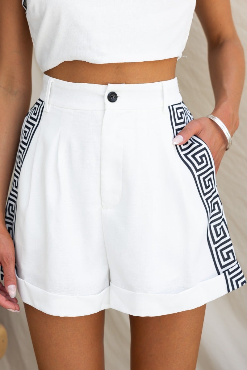Stylish white shorts with decorative black geometric pattern and pockets, featuring a mid-high waist fit.