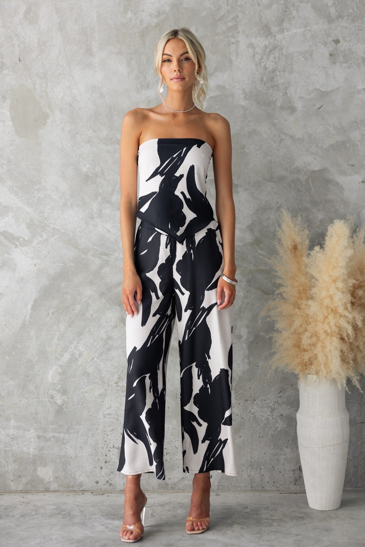 Model showcasing Yanna Pants, black printed mid-high waist pants with pockets, styled with a strapless top.