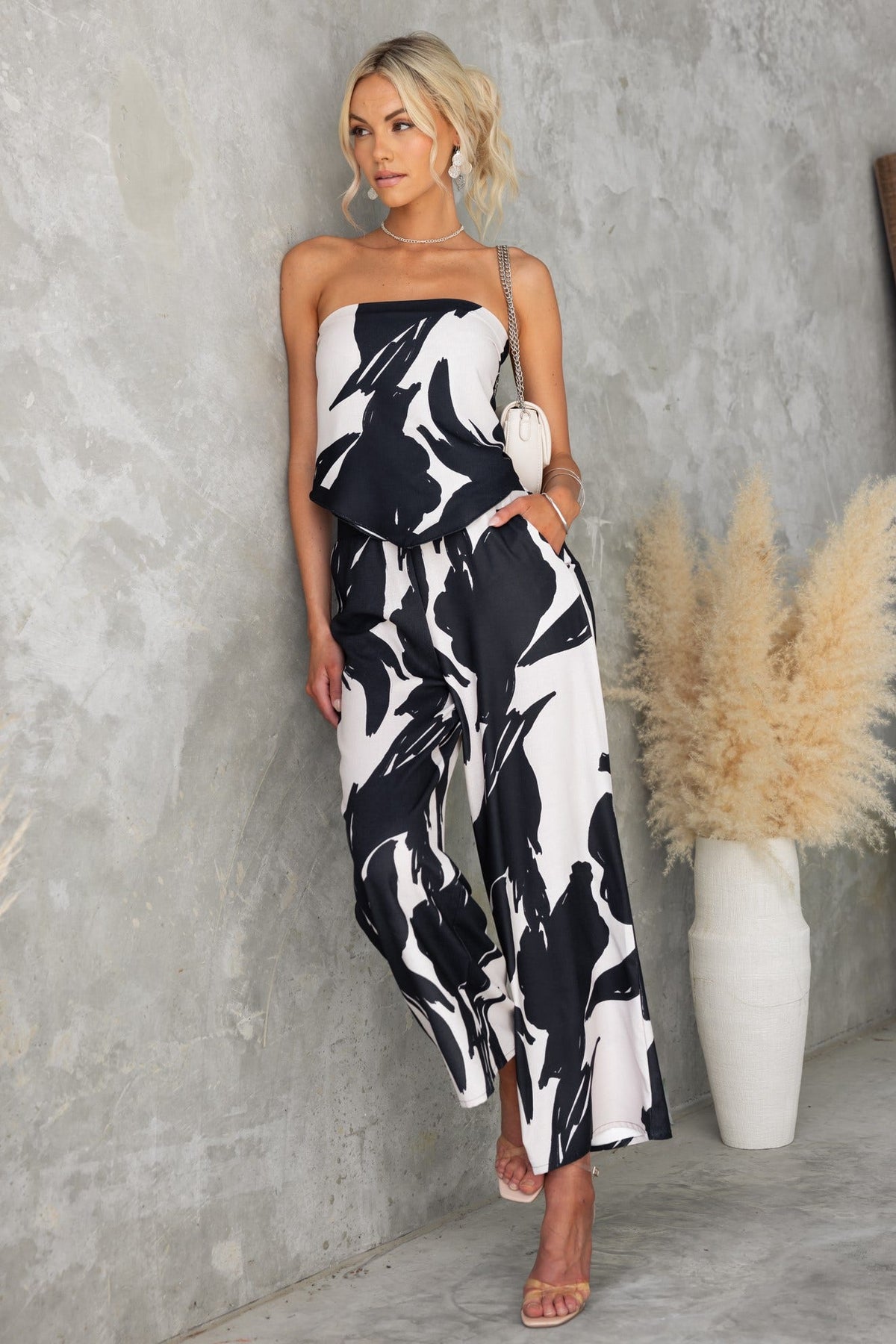 Stylish woman wearing Yanna Pants with black print, featuring mid-high waist and pockets, set against a textured wall.