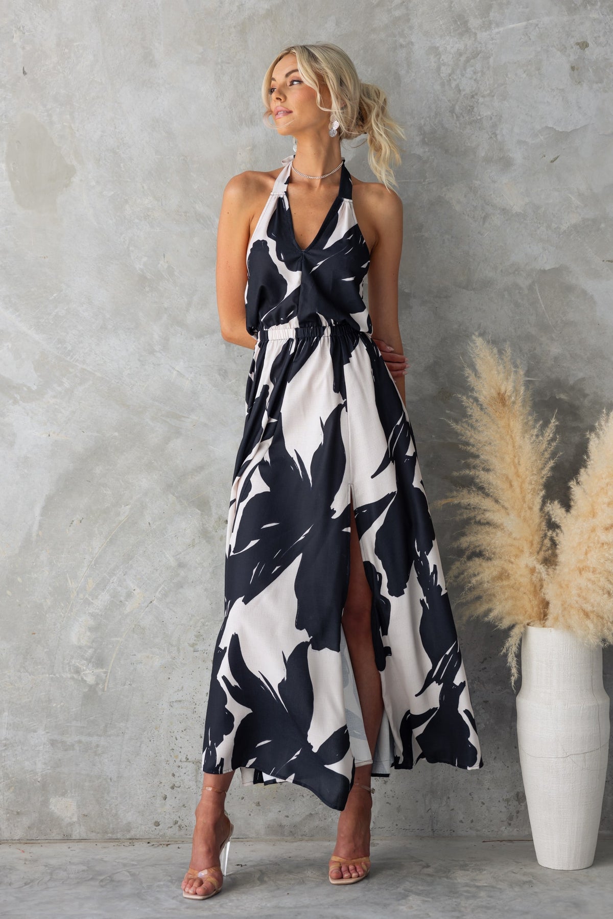 Model wearing a black and white floral print Casilda maxi dress with adjustable tie neckline and front split.
