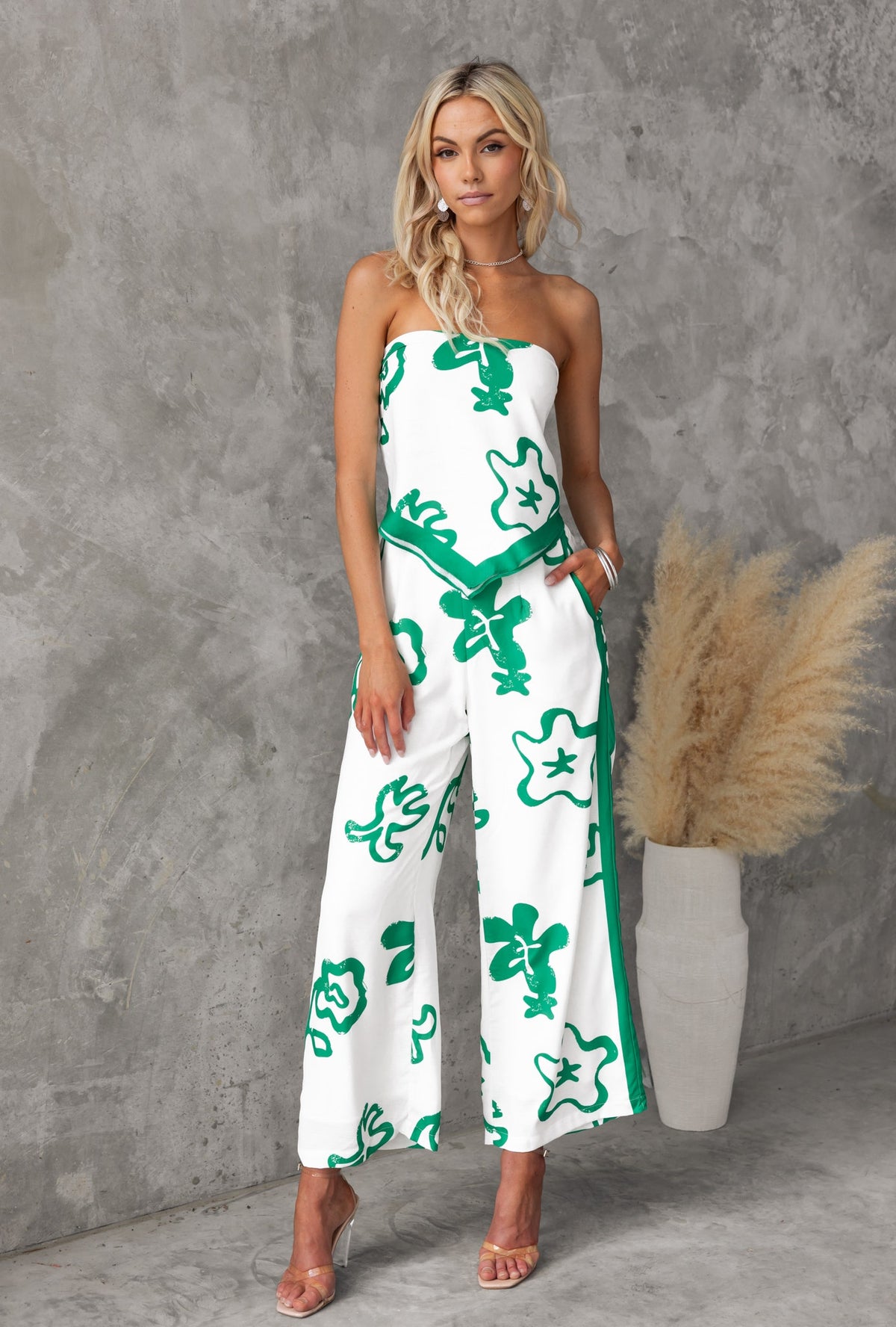 Model in a green and white floral print strapless jumpsuit styled with minimal accessories.