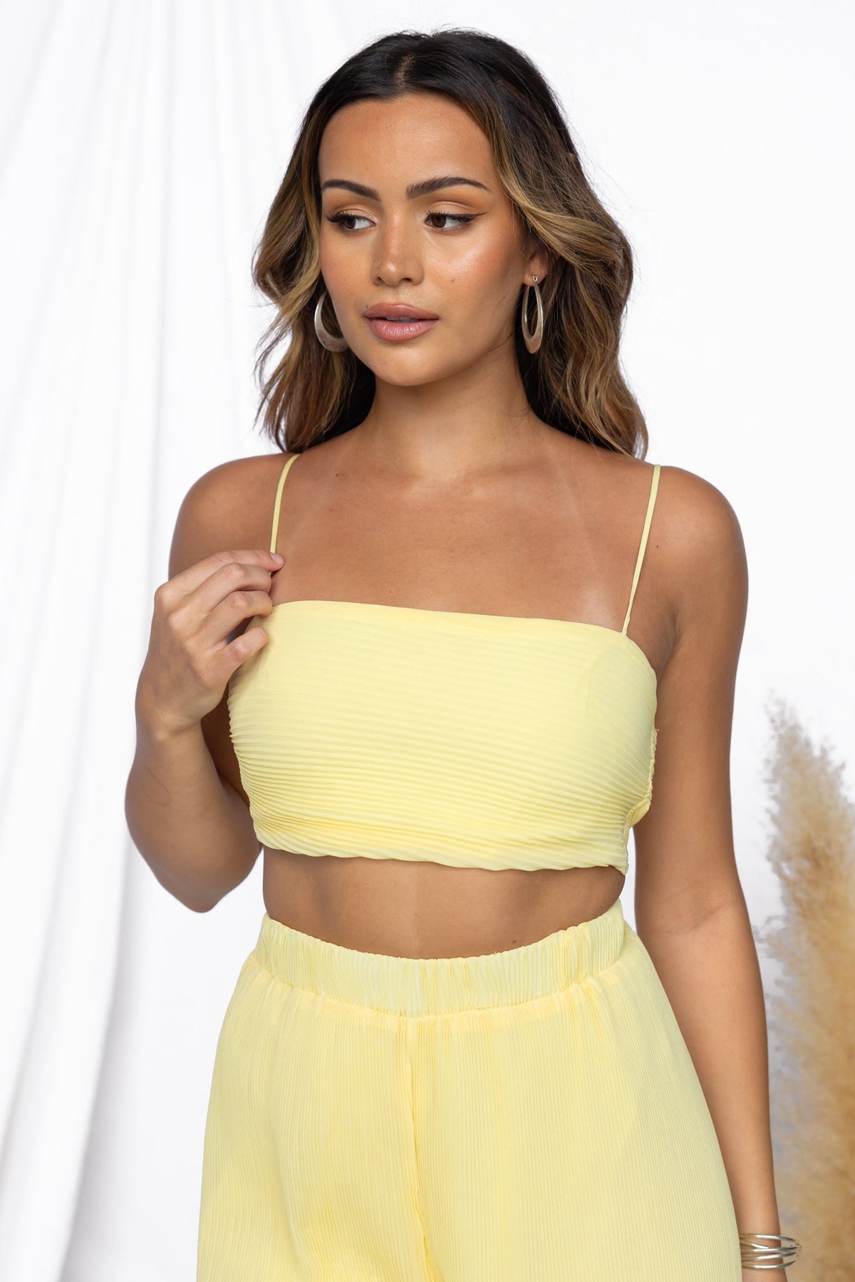 Model showcasing the Elida Top in yellow, featuring adjustable straps and pleated material.