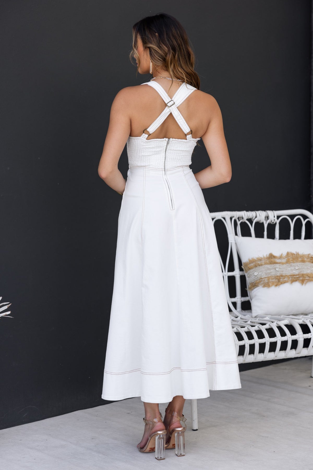 Back view of a woman wearing a white denim midi dress with adjustable straps and a zip closure.