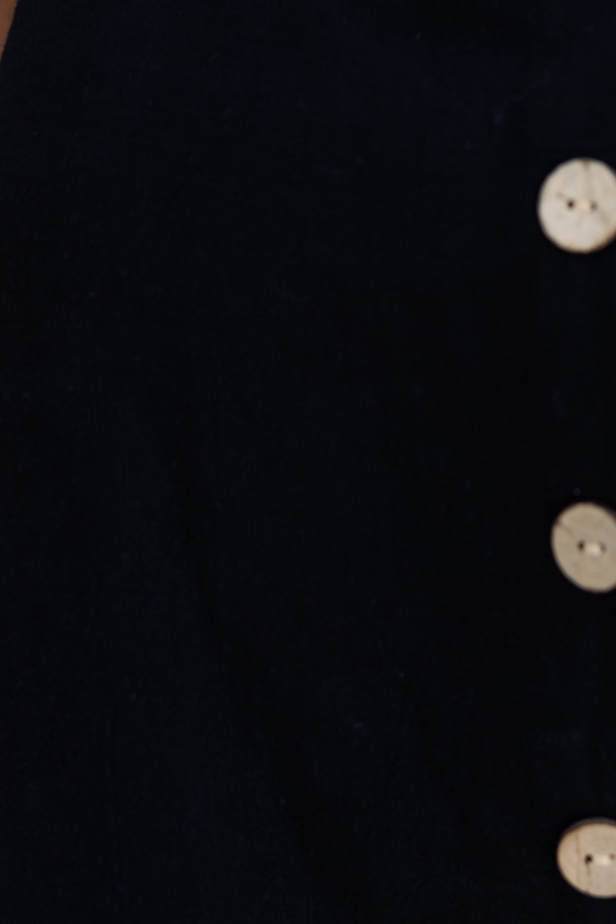 Close-up of Jaye Top featuring a black fabric with faux buttons and a square neckline.