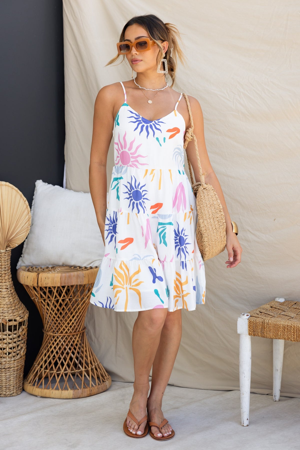 Woman wearing Romee Dress with abstract floral print, adjustable straps, and linen look, posing in a stylish setting.