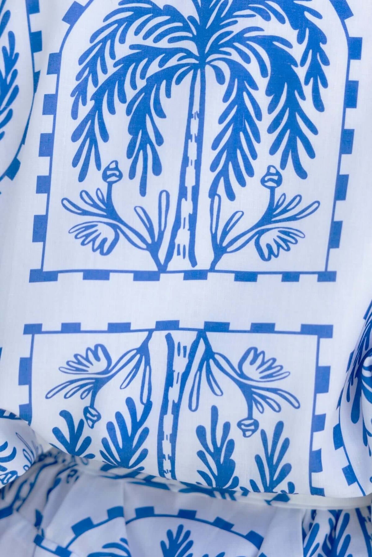 Close-up of blue palm and floral print on white fabric of the Alli Playsuit, showcasing intricate design details.