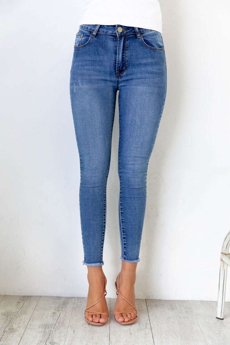 Juicebox Jeans - Mid waist, small distressed details, raw hem, stretchy denim material, standard skinny fit.
