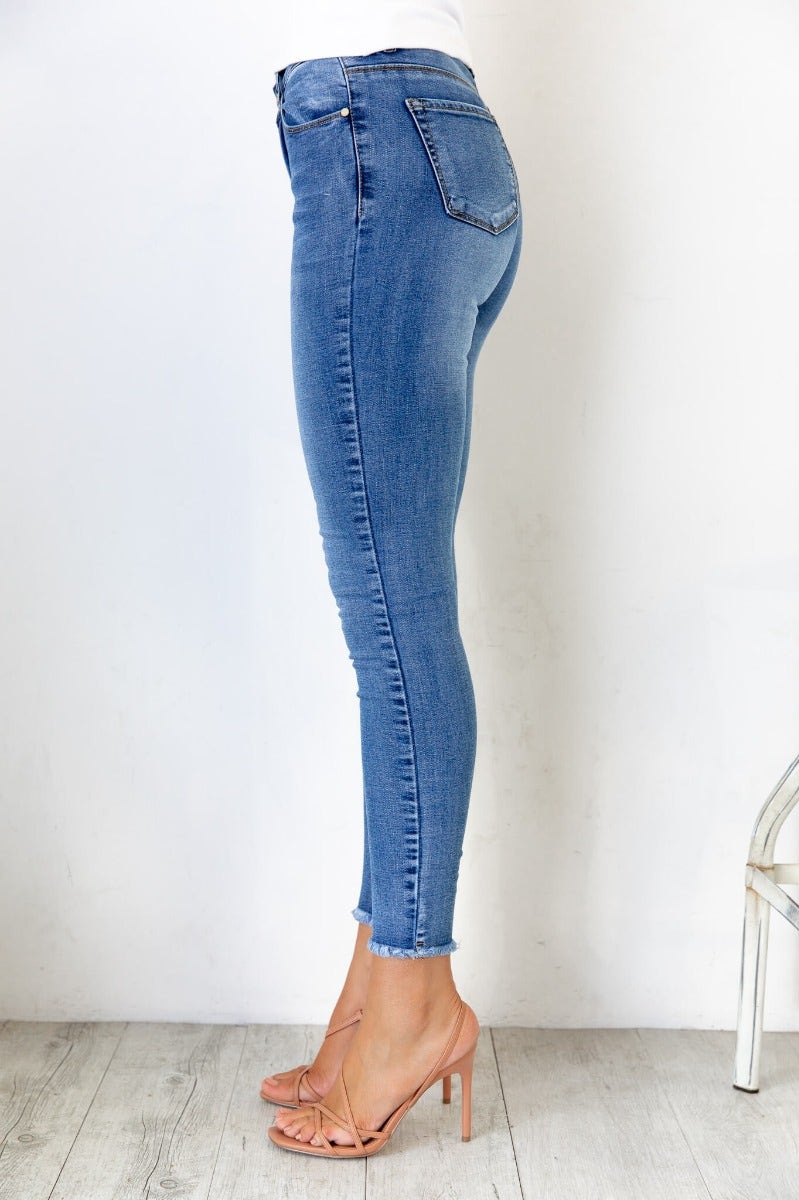Side view of Juicebox Jeans featuring mid waist fit, distressed details, and raw hem, styled with strappy heels.