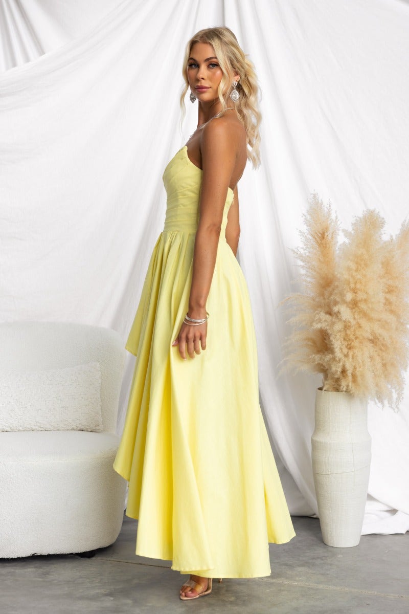 Model wearing a yellow Kiss And Tell Maxi Dress, showcasing a strapless design with an asymmetric hem and elegant silhouette.