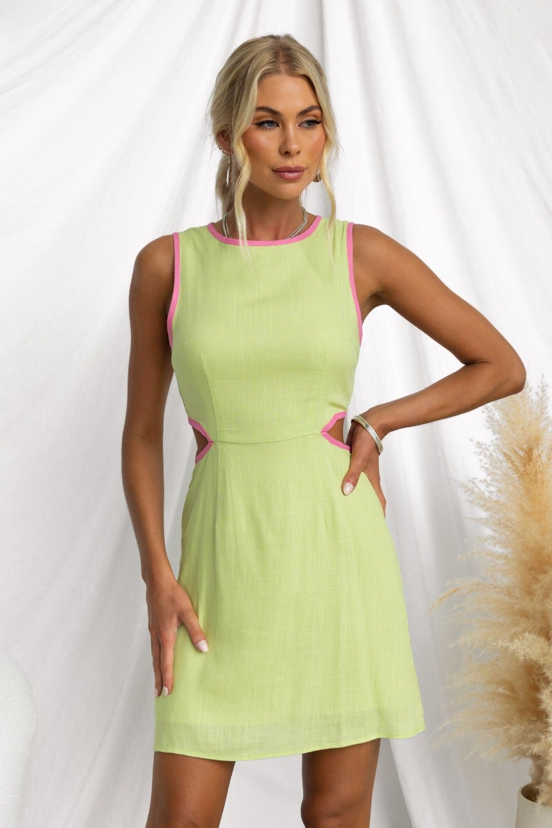 Model wearing a stylish Inside Out Mini Dress in light green with pink trim and cut-out details.