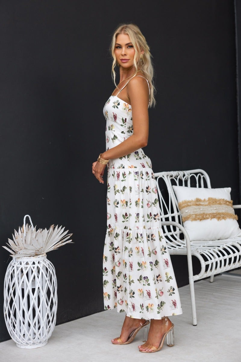 Carlyle Maxi Dress featuring floral print and adjustable straps, styled in a chic outdoor setting.