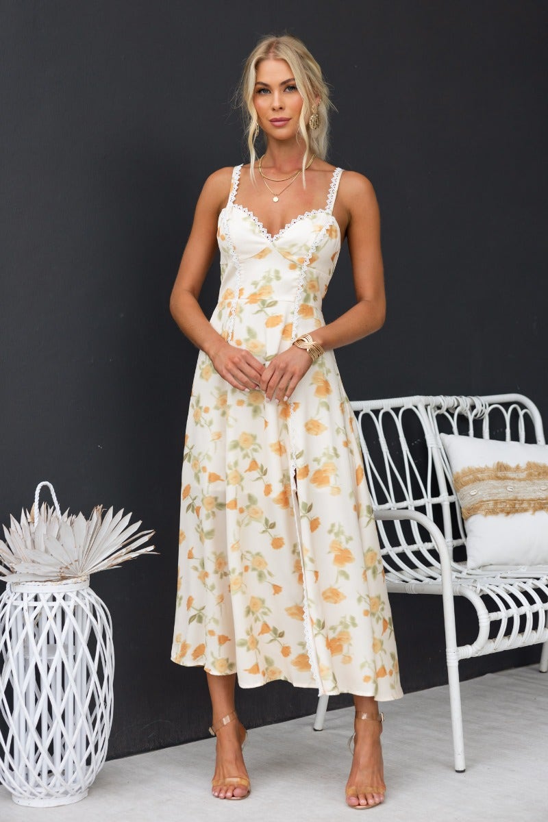 Model wearing Brigita Midi Dress with floral print, adjustable straps, and lace detailing, styled with minimal accessories.