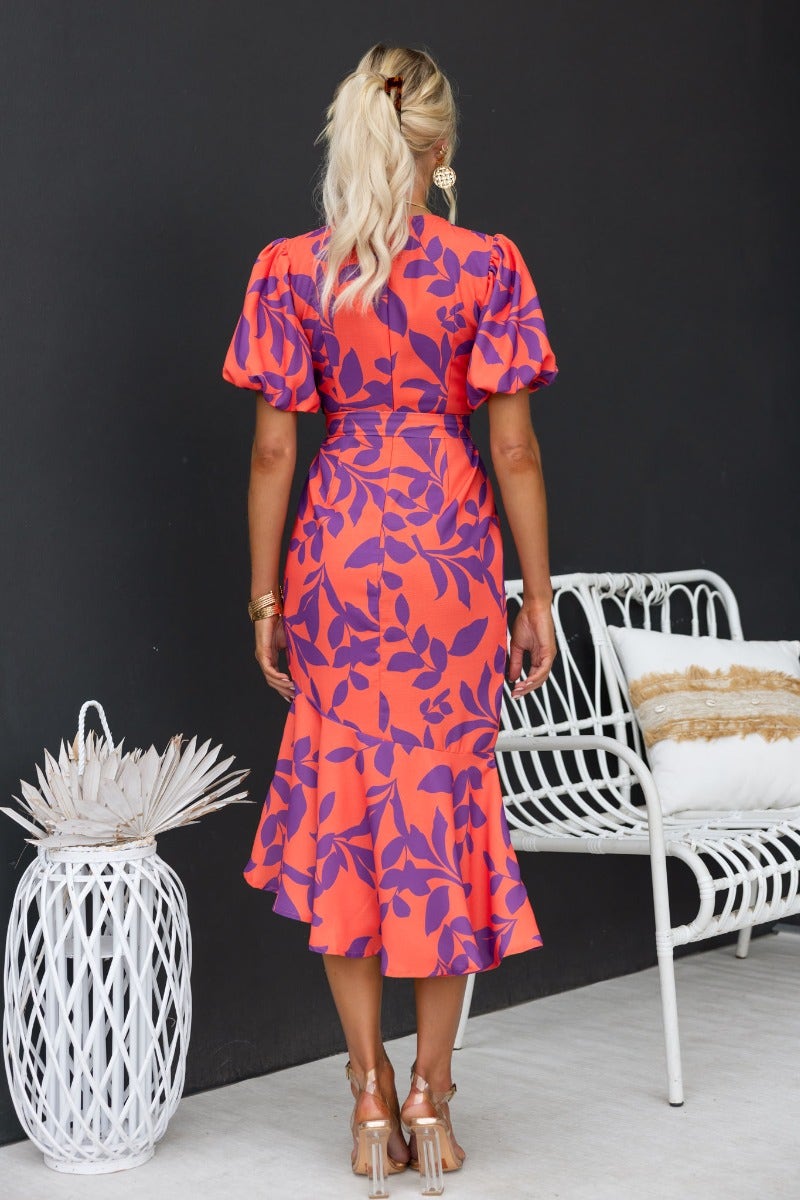 Back view of a floral print Linus Midi Dress with puff sleeves and a ruffled hem, styled with a modern chair.