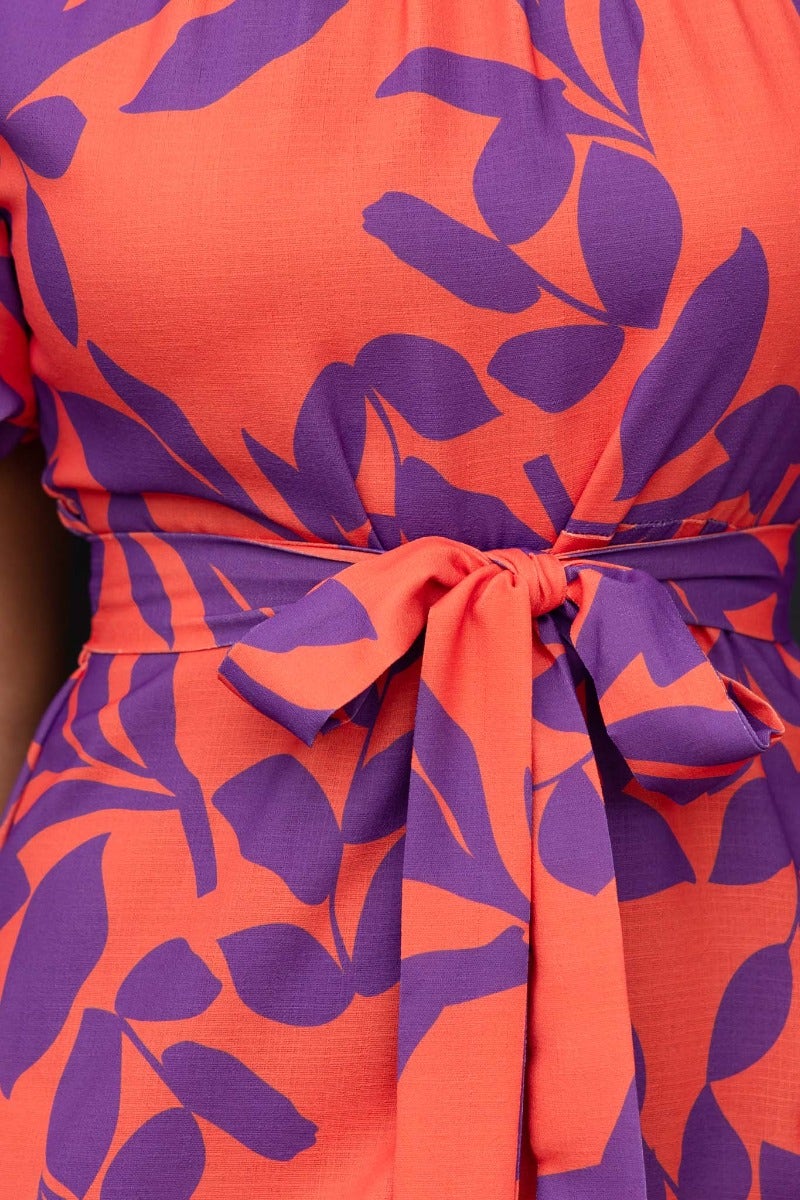 Close-up of Linus Midi Dress featuring vibrant orange fabric with purple leaf print and a stylish fabric tie detail.