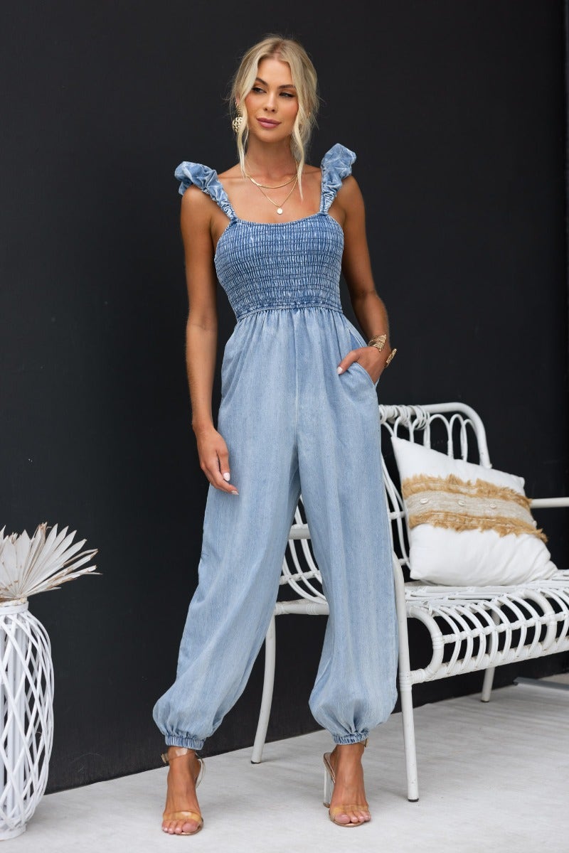 Model wearing the Paddington denim jumpsuit featuring elastic bodice, wide legs, and ruffle straps.