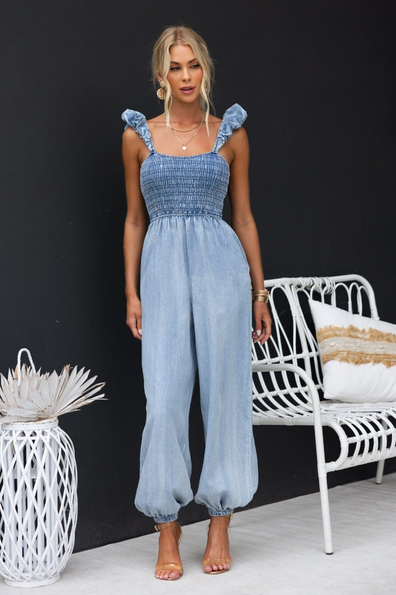Paddington Denim Jumpsuit featuring a smocked bodice, elastic ankle cuffs, and wide legs in soft denim fabric.