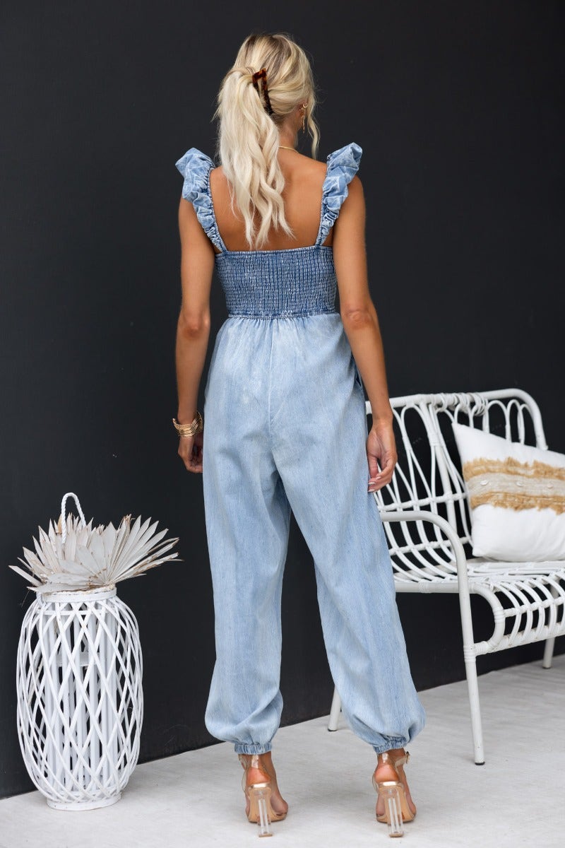 Woman wearing a Paddington Denim Jumpsuit with ruffled straps and wide legs, showcasing a stylish back view.