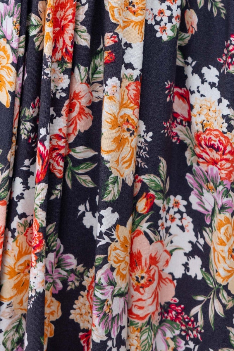 Close-up of floral print fabric featuring vibrant orange, pink, and white flowers on a dark background.